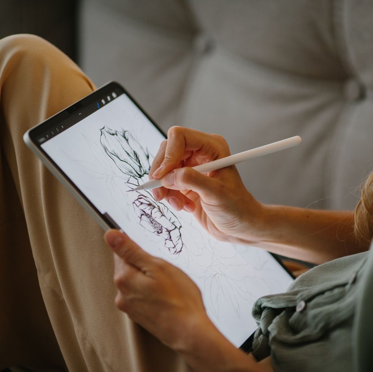 Woman drawing on a digital tablet resting on her knee.